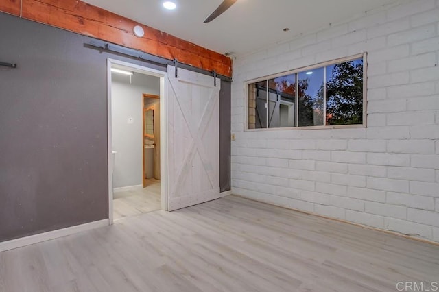 empty room with a barn door, wood finished floors, a ceiling fan, and baseboards