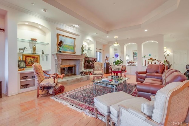 living area featuring light wood finished floors, built in features, a glass covered fireplace, a tray ceiling, and recessed lighting