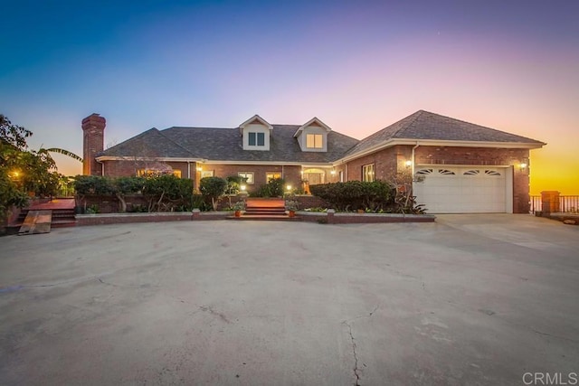 new england style home featuring driveway, a garage, and brick siding