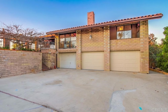 view of front of home featuring an attached garage, a balcony, a chimney, and concrete driveway