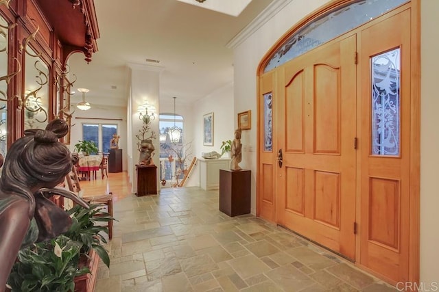 foyer featuring an inviting chandelier, stone tile floors, visible vents, and crown molding