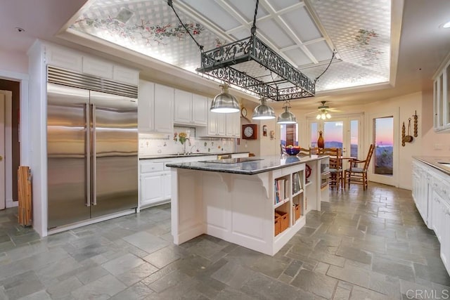 kitchen with stainless steel built in fridge, a kitchen island, white cabinets, decorative backsplash, and stone tile flooring