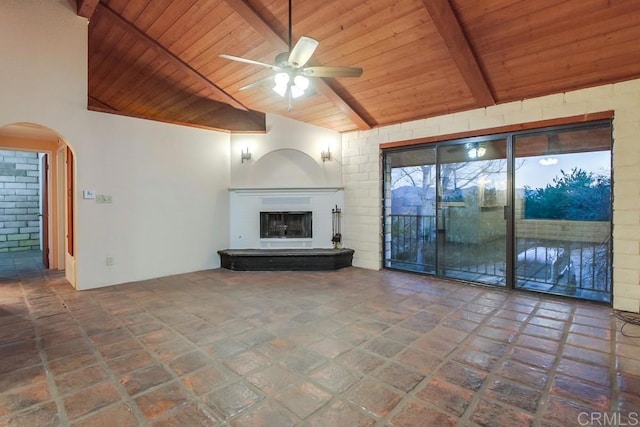 unfurnished living room with a ceiling fan, arched walkways, wood ceiling, and a fireplace with raised hearth