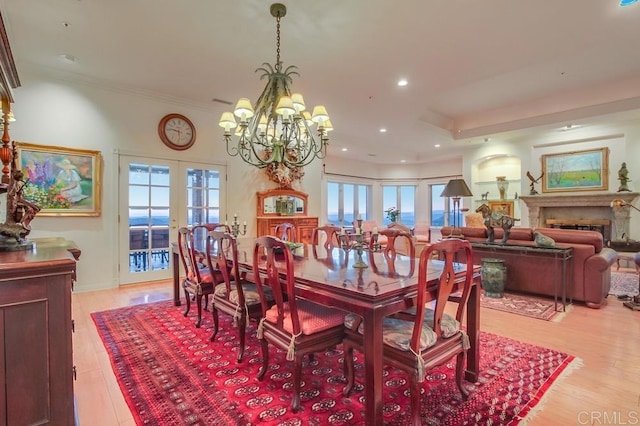 dining area with light wood-style floors, plenty of natural light, a fireplace, and a notable chandelier