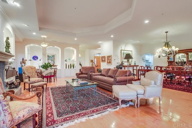 living room featuring arched walkways, a raised ceiling, wood finished floors, a chandelier, and recessed lighting