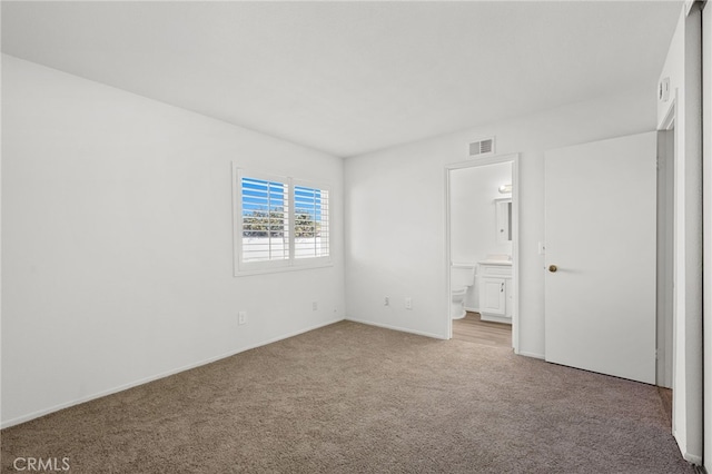 unfurnished bedroom featuring ensuite bath, carpet flooring, and visible vents