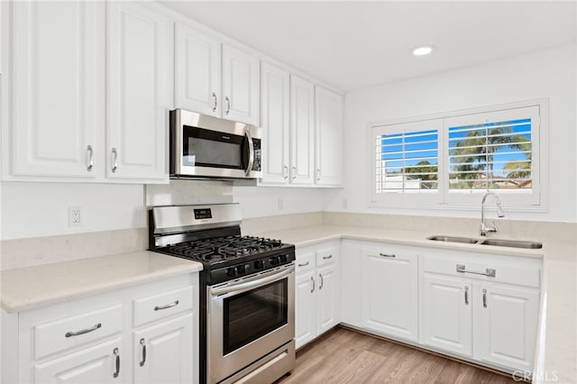 kitchen featuring stainless steel appliances, a sink, white cabinets, light countertops, and light wood-type flooring