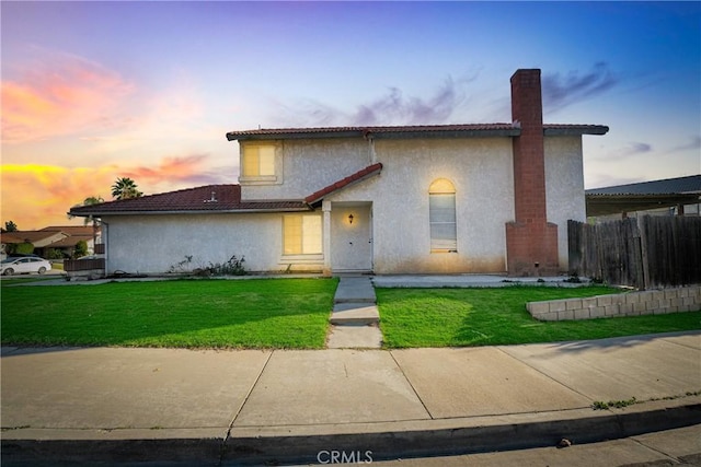 view of front facade with a yard, fence, a tiled roof, and stucco siding