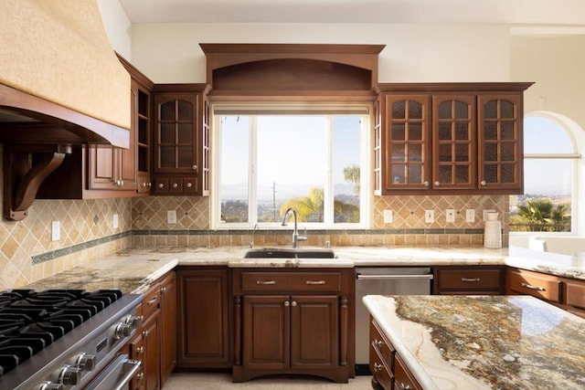 kitchen featuring tasteful backsplash, glass insert cabinets, appliances with stainless steel finishes, light stone counters, and a sink