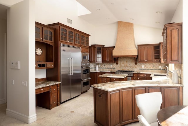 kitchen with built in appliances, a peninsula, a sink, premium range hood, and backsplash