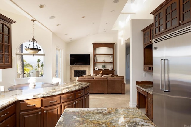 kitchen featuring vaulted ceiling, a fireplace, built in fridge, and light stone countertops