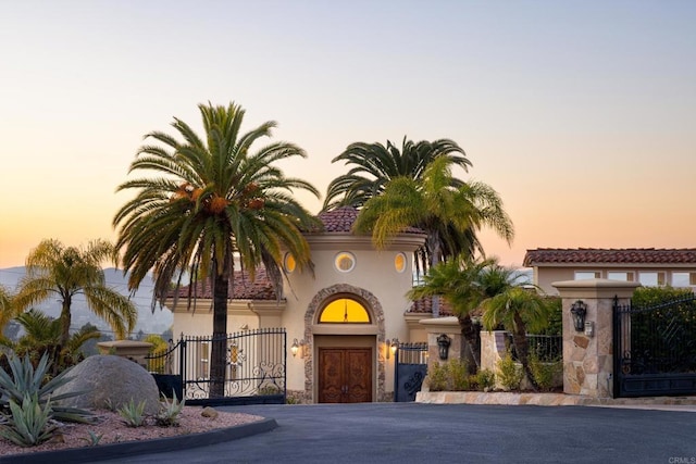 view of front of house with a tile roof, a gate, fence, and stucco siding