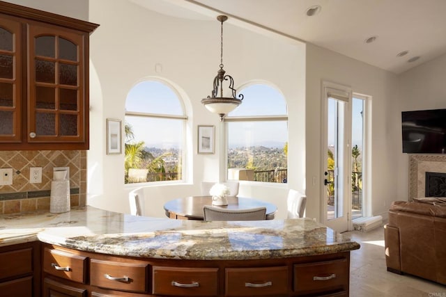 kitchen with light stone counters, a fireplace, open floor plan, tasteful backsplash, and glass insert cabinets