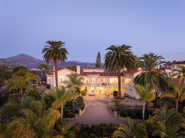 back of house at dusk featuring a mountain view, a balcony, and stucco siding