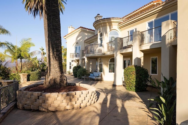 exterior space with a chimney, stucco siding, a patio area, a balcony, and a tiled roof