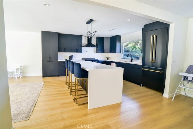 kitchen featuring high end refrigerator, light wood-style flooring, a kitchen island, light countertops, and wall chimney range hood