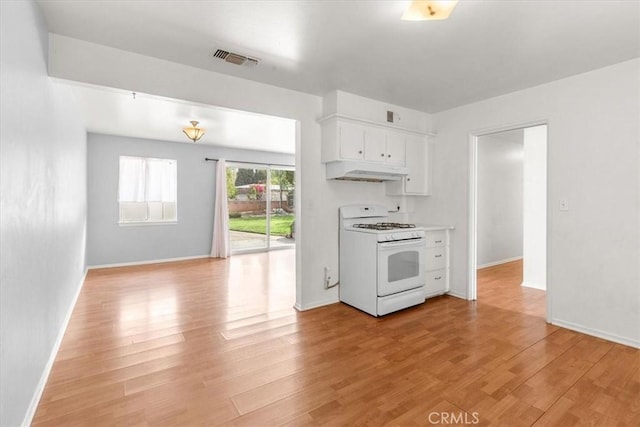 kitchen featuring light wood-style floors, white cabinetry, under cabinet range hood, and white gas range