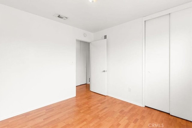 unfurnished bedroom featuring light wood-type flooring, a closet, visible vents, and baseboards