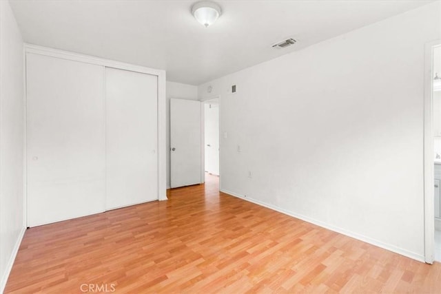 unfurnished bedroom with light wood finished floors, baseboards, visible vents, and a closet