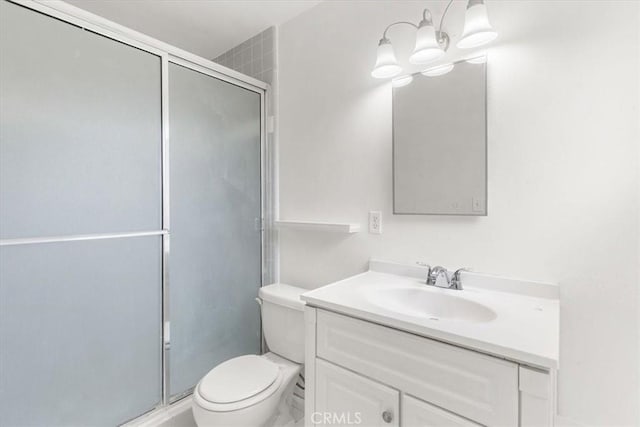 bathroom with a stall shower, vanity, toilet, and an inviting chandelier