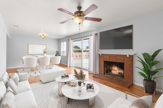 living room with ceiling fan, a fireplace, wood finished floors, and baseboards