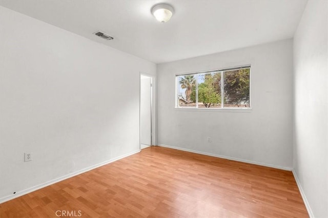 spare room with light wood-type flooring, visible vents, and baseboards