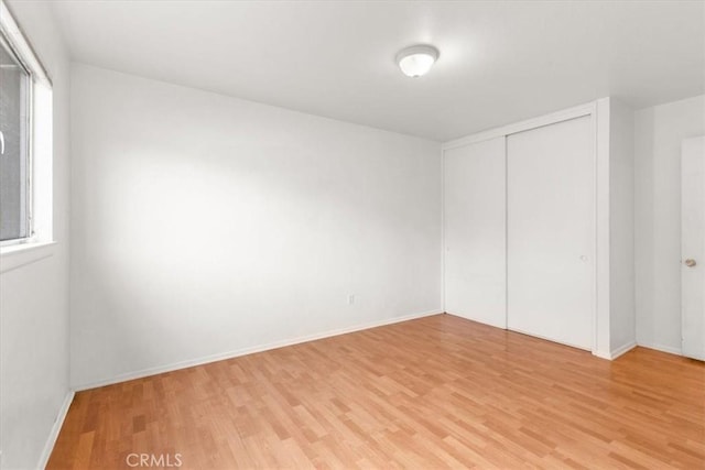 unfurnished bedroom with a closet, baseboards, and light wood finished floors