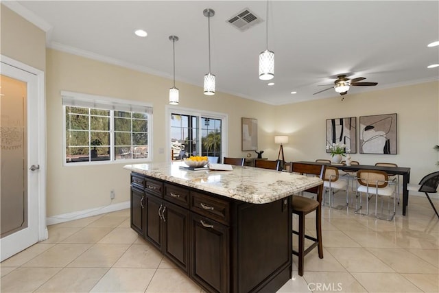 kitchen featuring a breakfast bar, pendant lighting, light tile patterned floors, visible vents, and ornamental molding