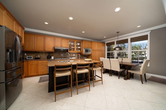 kitchen with stainless steel appliances, brown cabinetry, a sink, and backsplash