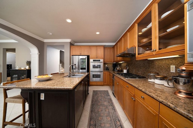 kitchen featuring light tile patterned floors, arched walkways, stainless steel appliances, under cabinet range hood, and a sink