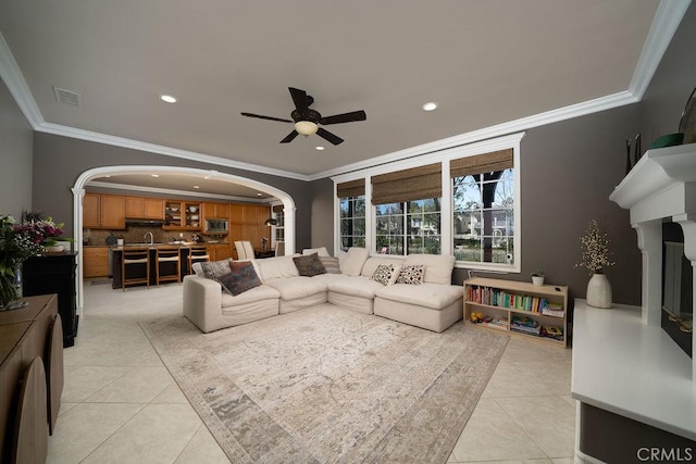 living area featuring arched walkways, ornamental molding, a ceiling fan, and light tile patterned flooring