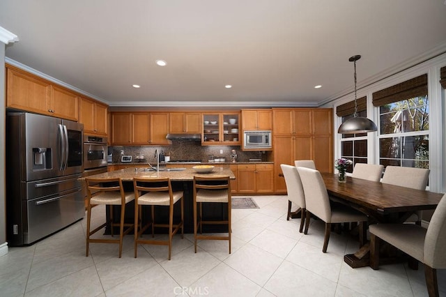 kitchen featuring under cabinet range hood, stainless steel appliances, ornamental molding, brown cabinets, and tasteful backsplash