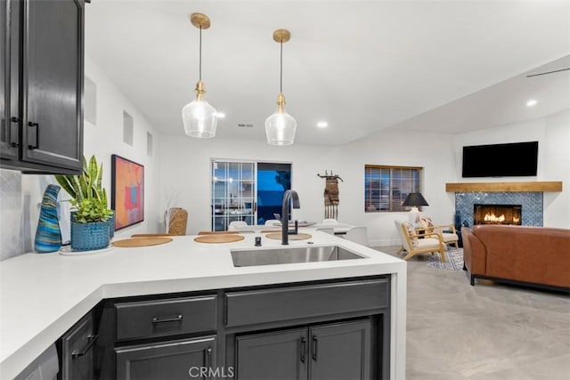 kitchen with a peninsula, a sink, open floor plan, light countertops, and a lit fireplace