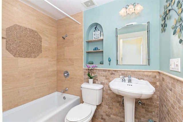 full bath with toilet, wainscoting, tile walls, visible vents, and washtub / shower combination
