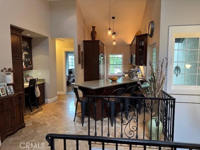 kitchen with high vaulted ceiling, pendant lighting, glass insert cabinets, baseboards, and dark brown cabinets