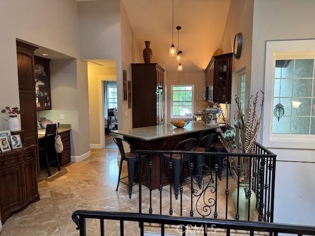 kitchen with a high ceiling, pendant lighting, dark brown cabinetry, glass insert cabinets, and fridge