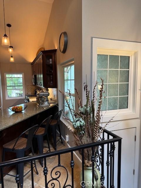 kitchen with glass insert cabinets, pendant lighting, dark brown cabinetry, tasteful backsplash, and high vaulted ceiling