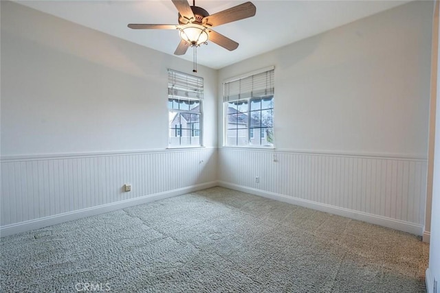 carpeted empty room featuring a ceiling fan and wainscoting