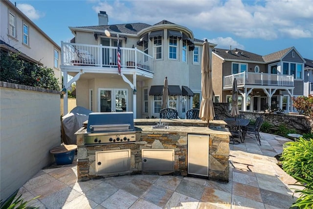 back of house with a patio, a balcony, a chimney, exterior kitchen, and stucco siding