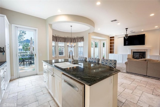 kitchen with a glass covered fireplace, stone tile flooring, stainless steel dishwasher, a sink, and recessed lighting