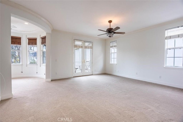 carpeted empty room with a ceiling fan, baseboards, and crown molding