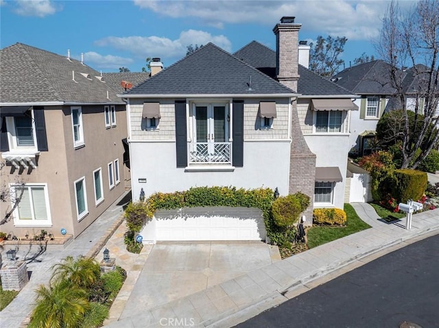 view of front facade with a chimney, stucco siding, a shingled roof, a garage, and driveway