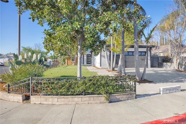 view of property hidden behind natural elements featuring driveway, a garage, and fence