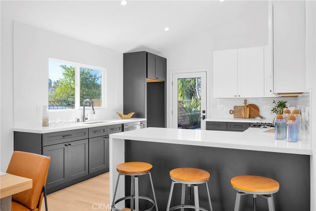 kitchen featuring a peninsula, a sink, light countertops, gray cabinets, and a kitchen bar