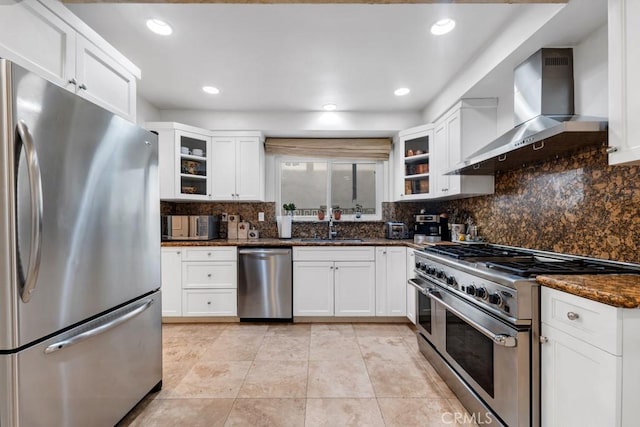 kitchen with tasteful backsplash, a sink, white cabinets, stainless steel appliances, and wall chimney exhaust hood