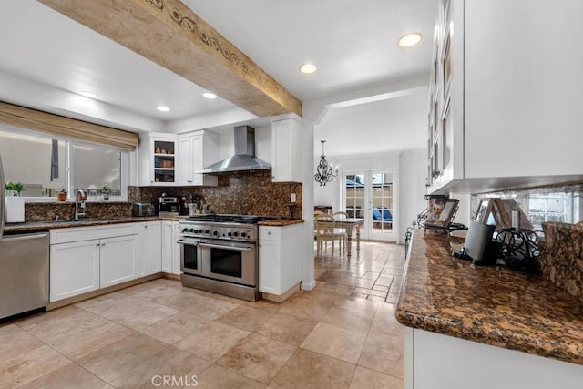 kitchen with decorative backsplash, wall chimney exhaust hood, white cabinetry, a sink, and appliances with stainless steel finishes