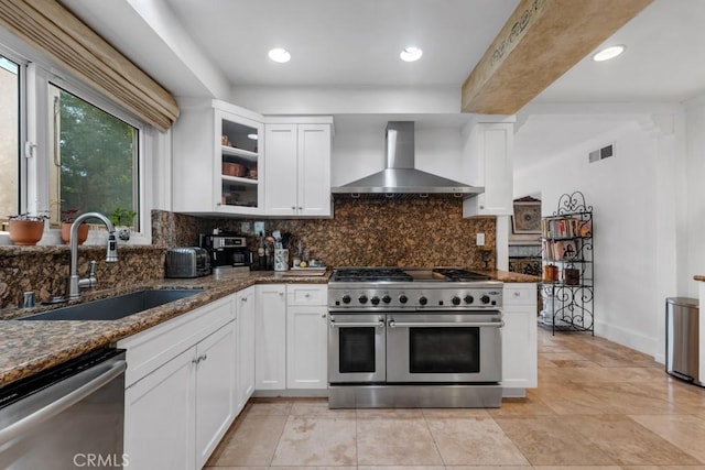 kitchen with visible vents, wall chimney range hood, a sink, dark stone countertops, and stainless steel appliances