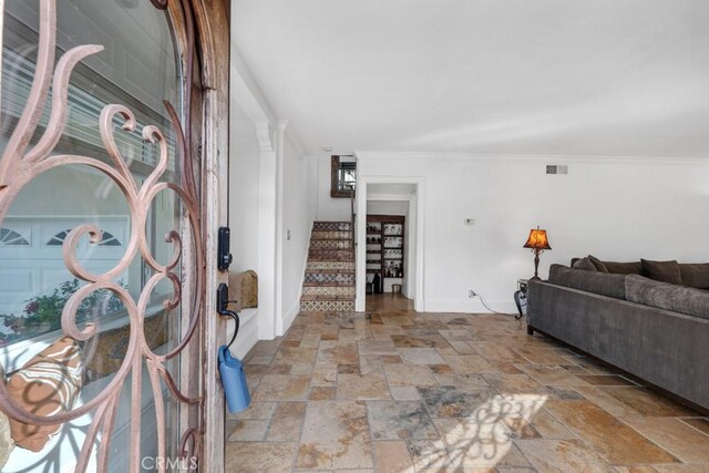 entrance foyer with stairs, baseboards, visible vents, ornamental molding, and stone tile flooring