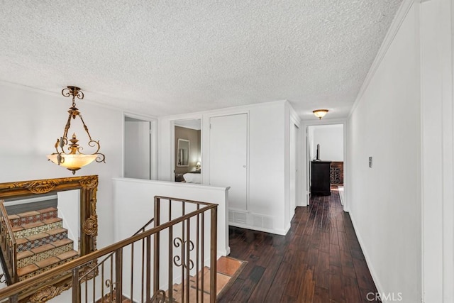 corridor with dark wood-style flooring, a textured ceiling, an upstairs landing, and visible vents