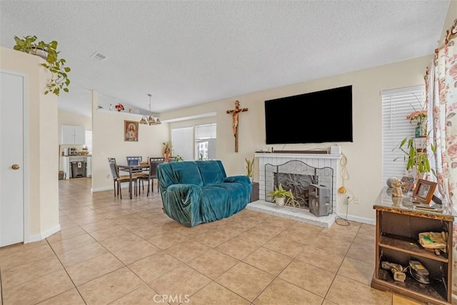 living area featuring light tile patterned floors, a textured ceiling, a brick fireplace, and baseboards